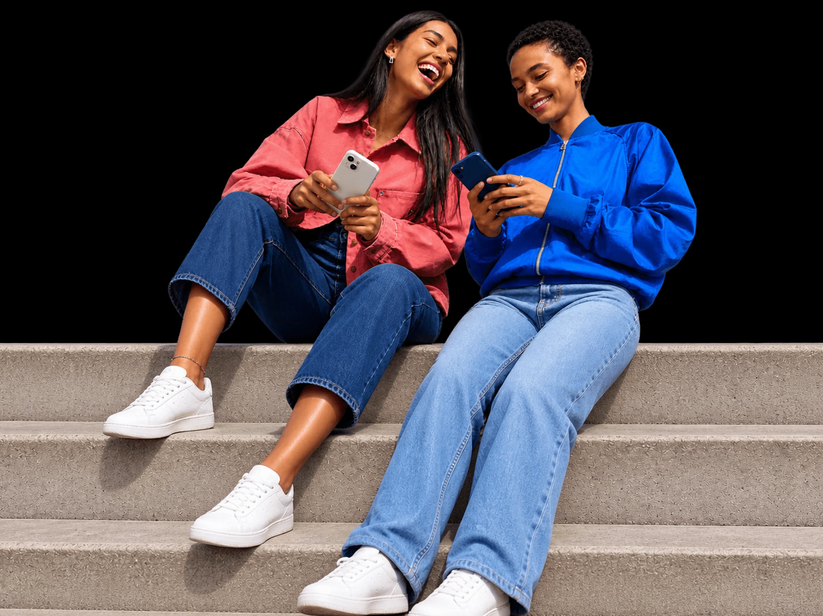 Two friends on a set of steps, laughing at something on their phones.